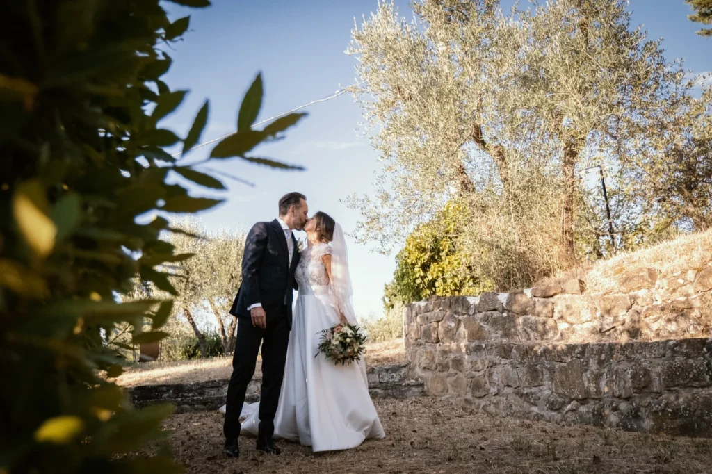 Bacio degli sposi tra gli ulivi accanto a un muretto in pietra