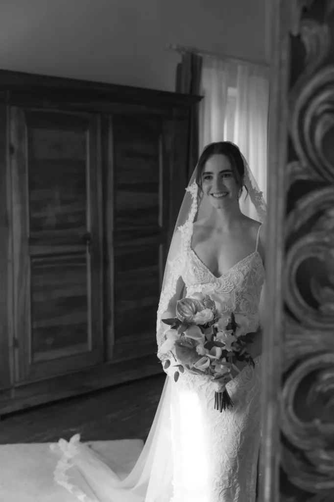 La sposa sorridente accanto alla finestra prima della cerimonia, in bianco e nero