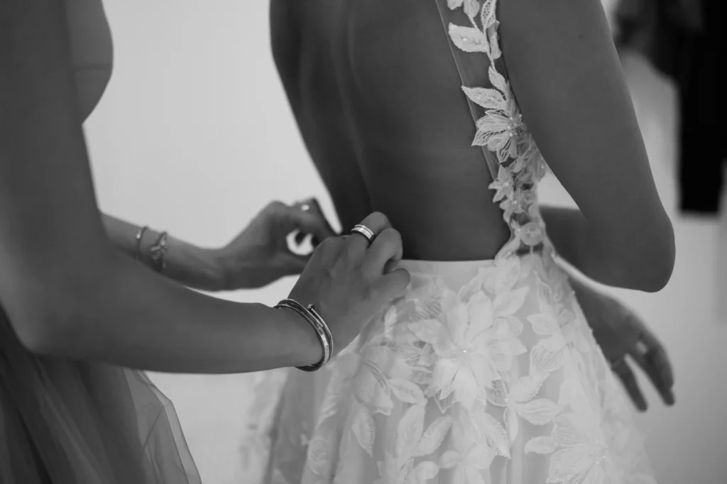 Mani che chiudono i bottoni dell'abito da sposa, in bianco e nero