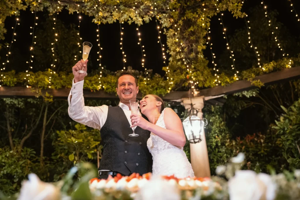 Sposi che brindano ridendo sotto una pergola illuminata