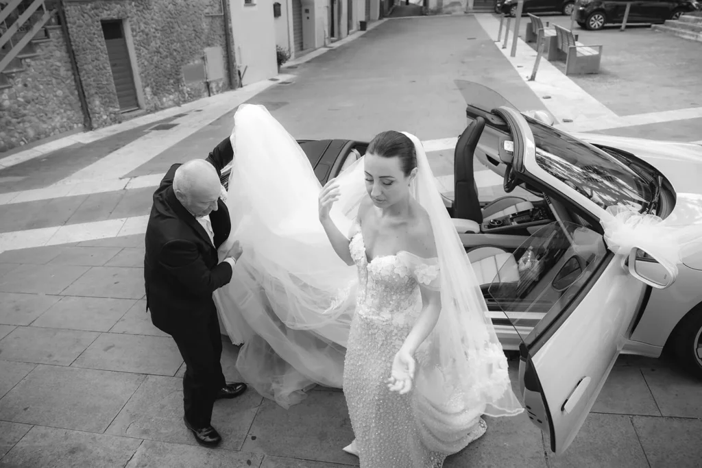 La sposa scende dall'auto con lo strascico, in bianco e nero