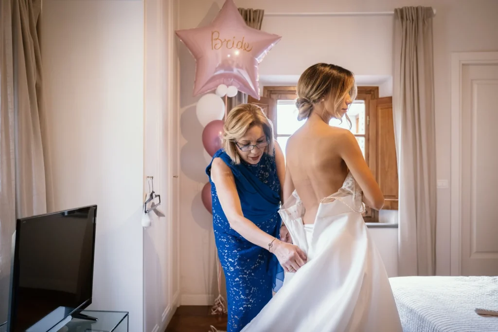 Una donna aiuta la sposa ad allacciare l'abito