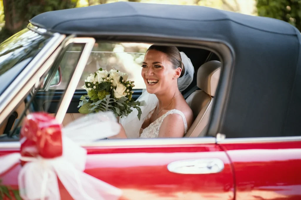Sposa sorridente sull'auto d'epoca rossa