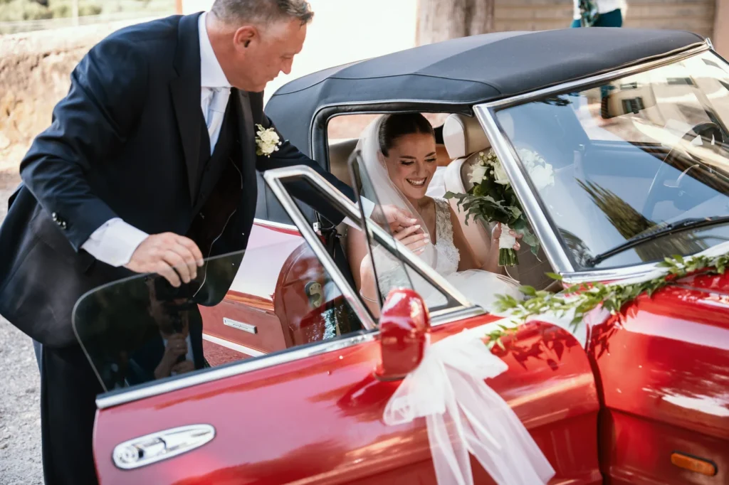 La portiera dell'auto d'epoca rossa si apre per la sposa