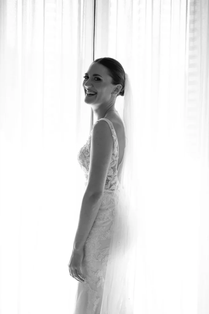 Sposa che ride in controluce tra le tende bianche