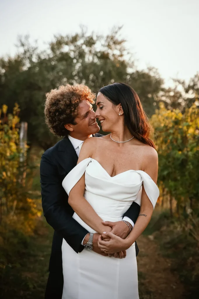 Sposo che abbraccia la sposa tra i filari al tramonto