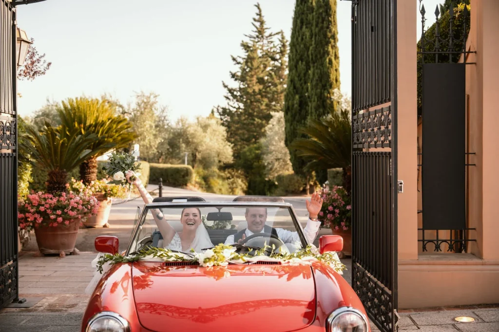 Sposi sull'auto d'epoca rossa all'ingresso della villa