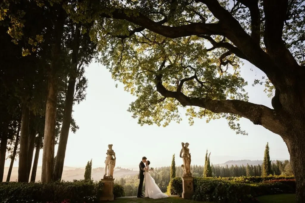 Sposi che si baciano tra le statue del giardino di una villa sotto una grande quercia