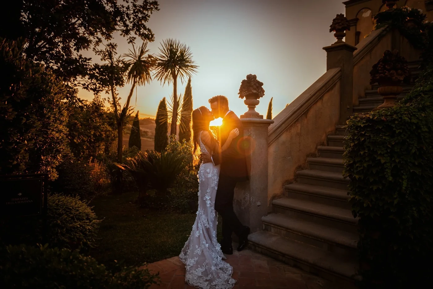 Sposi che si baciano in controluce al tramonto accanto alla scalinata di una villa