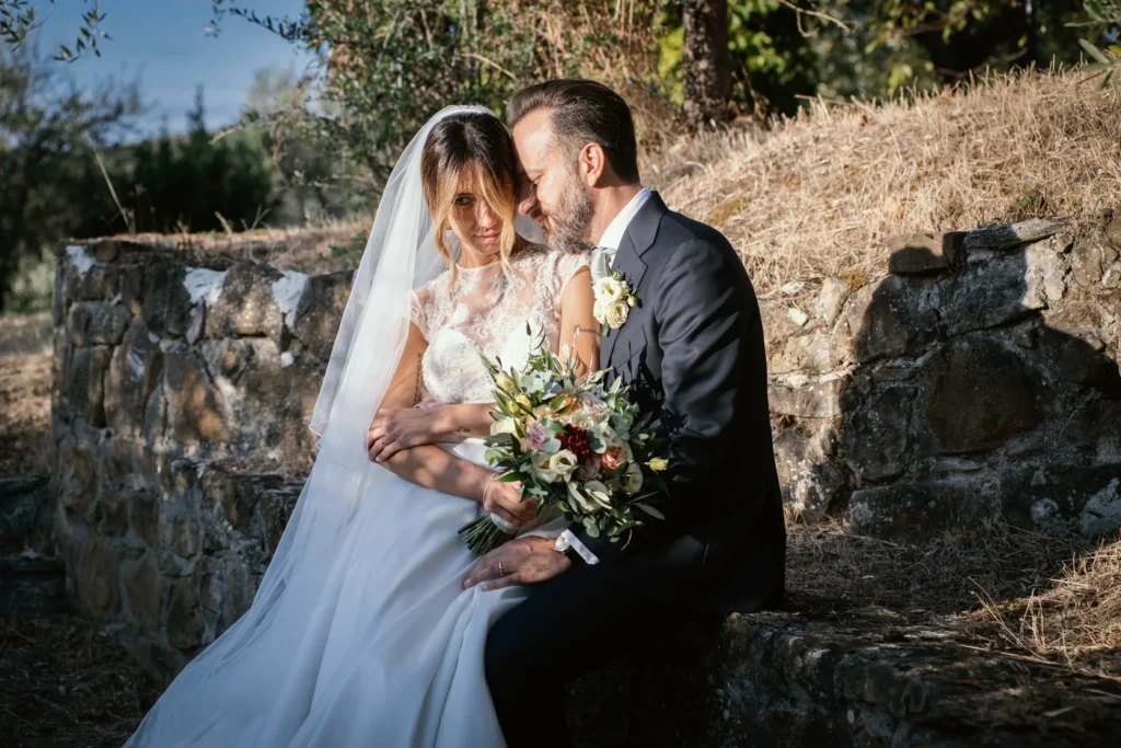 Sposi seduti su un muretto di pietra con il bouquet