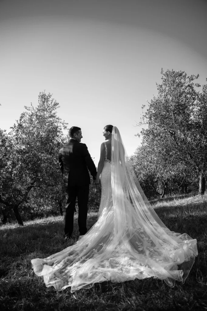 Sposi di spalle tra gli ulivi con il lungo velo, in bianco e nero