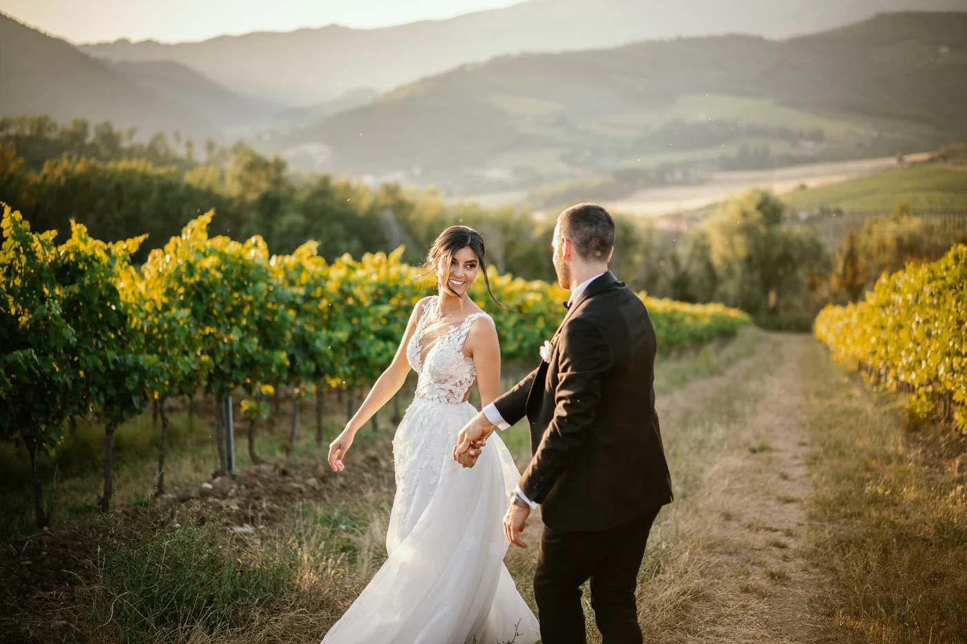 Sposi che si tengono per mano tra i vigneti in Toscana